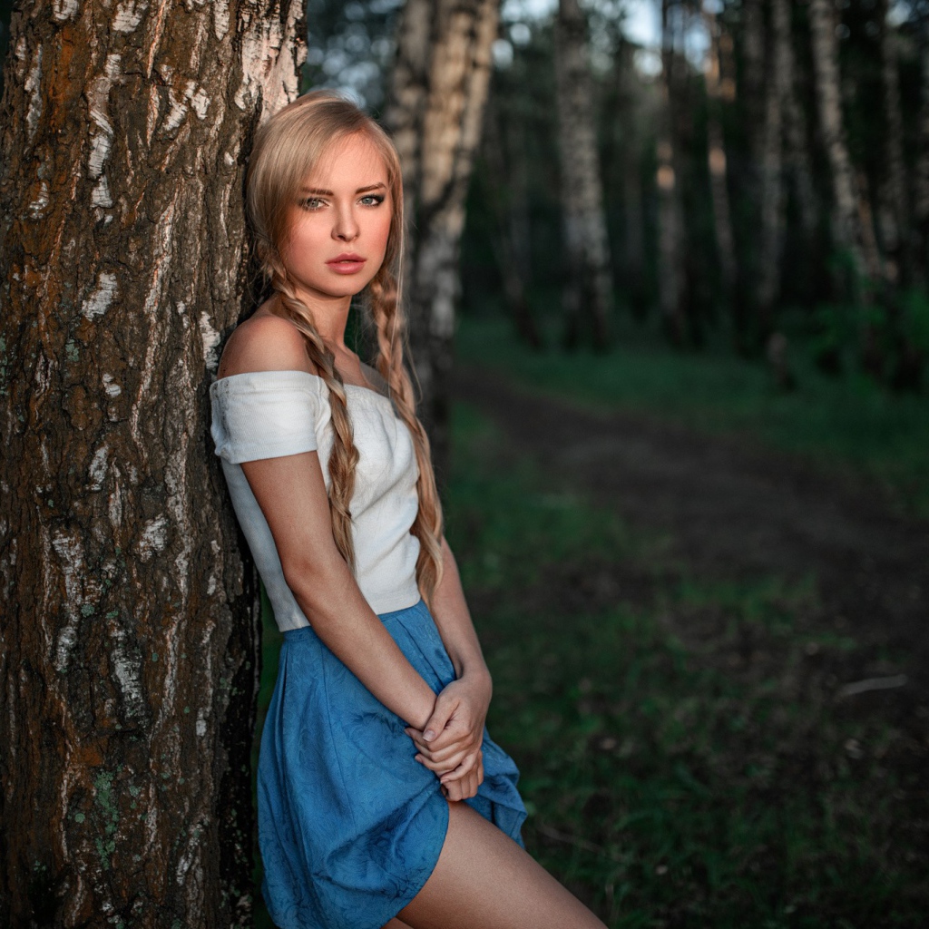 Девушка с русыми косами прислонилась к дереву