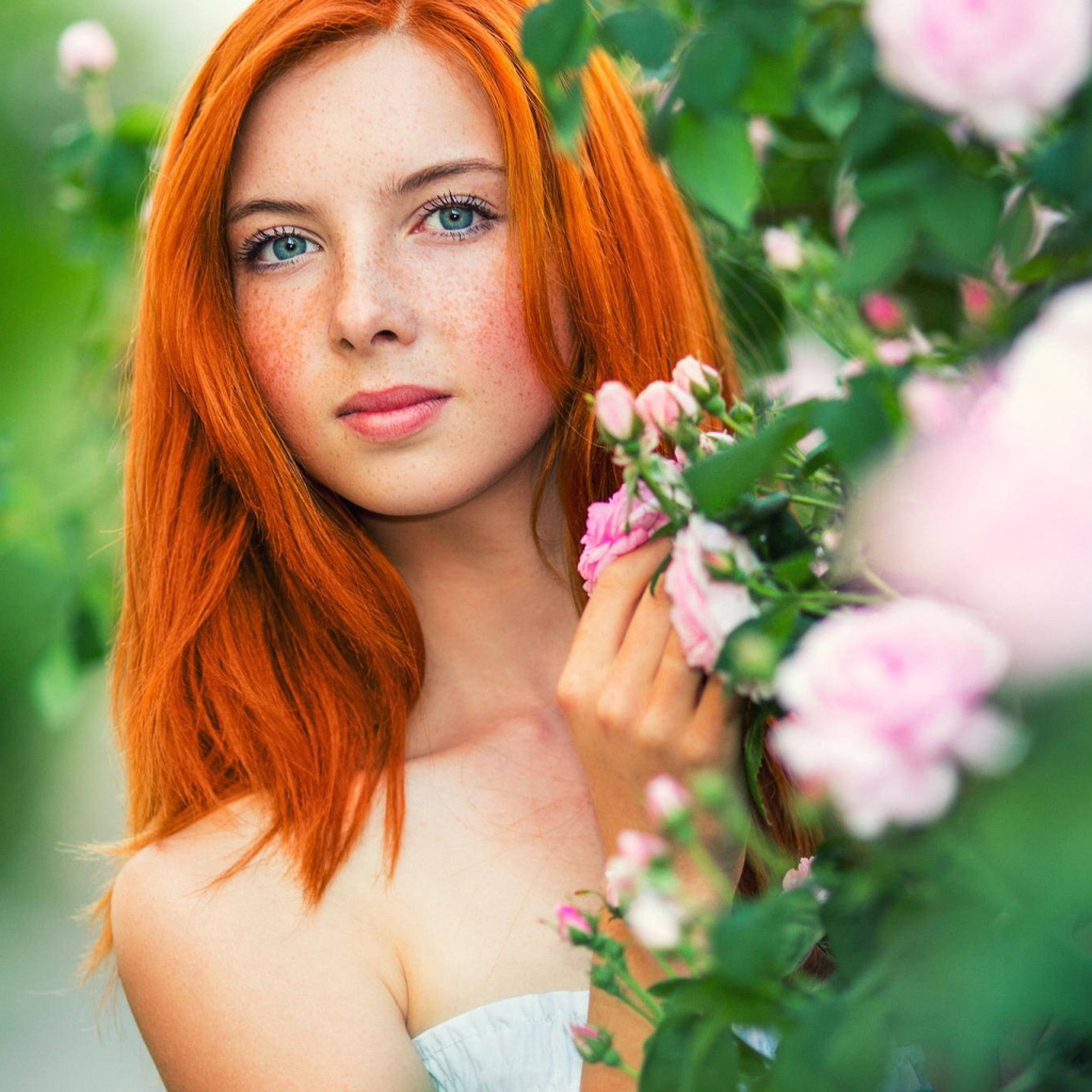 Red-haired girl hides behind the flowering branches