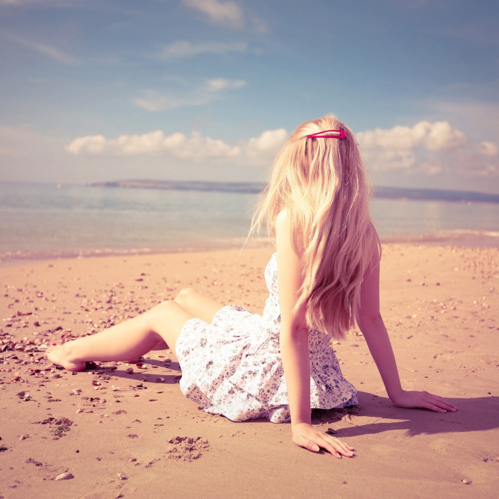 Блондинка с розовой заколкой сидит на пляже
