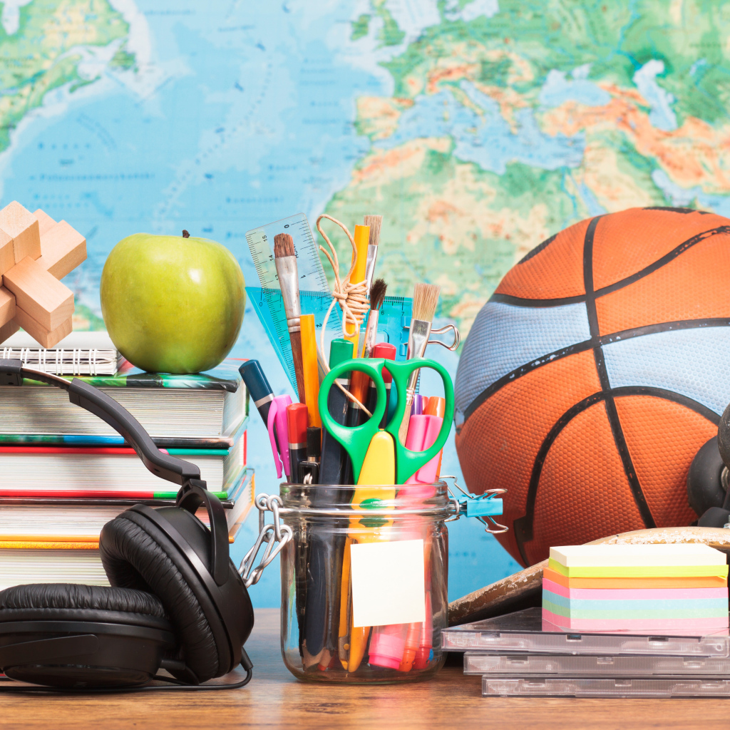 Мяч, наушники, книги и канцелярские принадлежности на столе на фоне карты