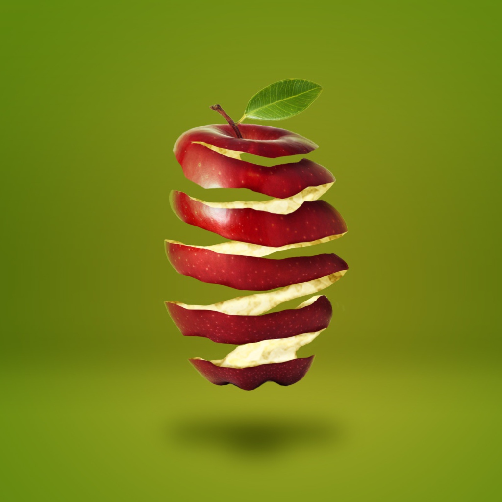 Нарезанное спиралью красное яблоко на зеленом фоне 