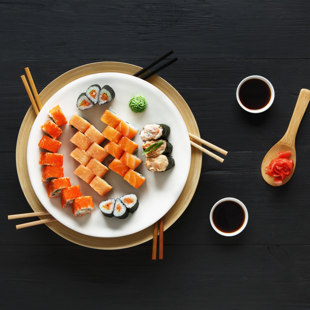 Суши и роллы на большой белой тарелке с соевым соусом