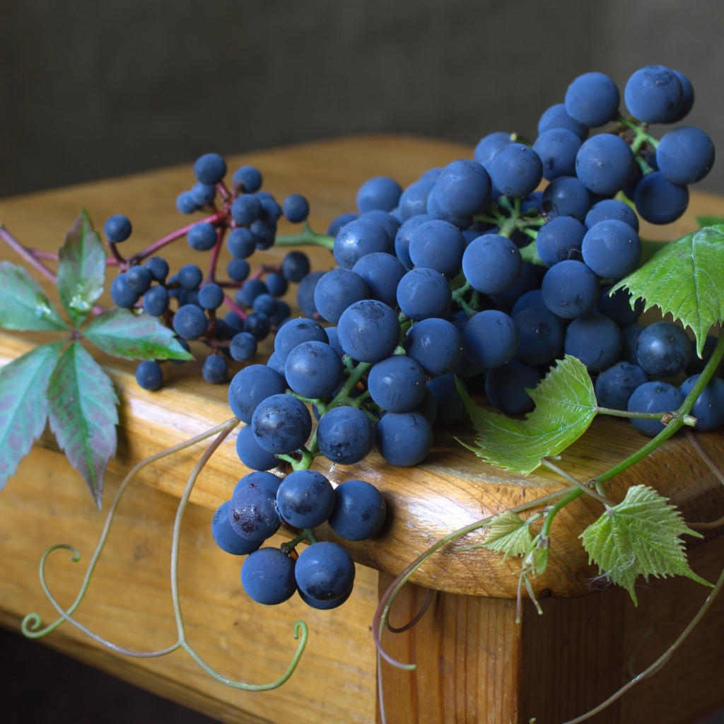 Синий виноград с зелеными листьями лежит на деревянном столе