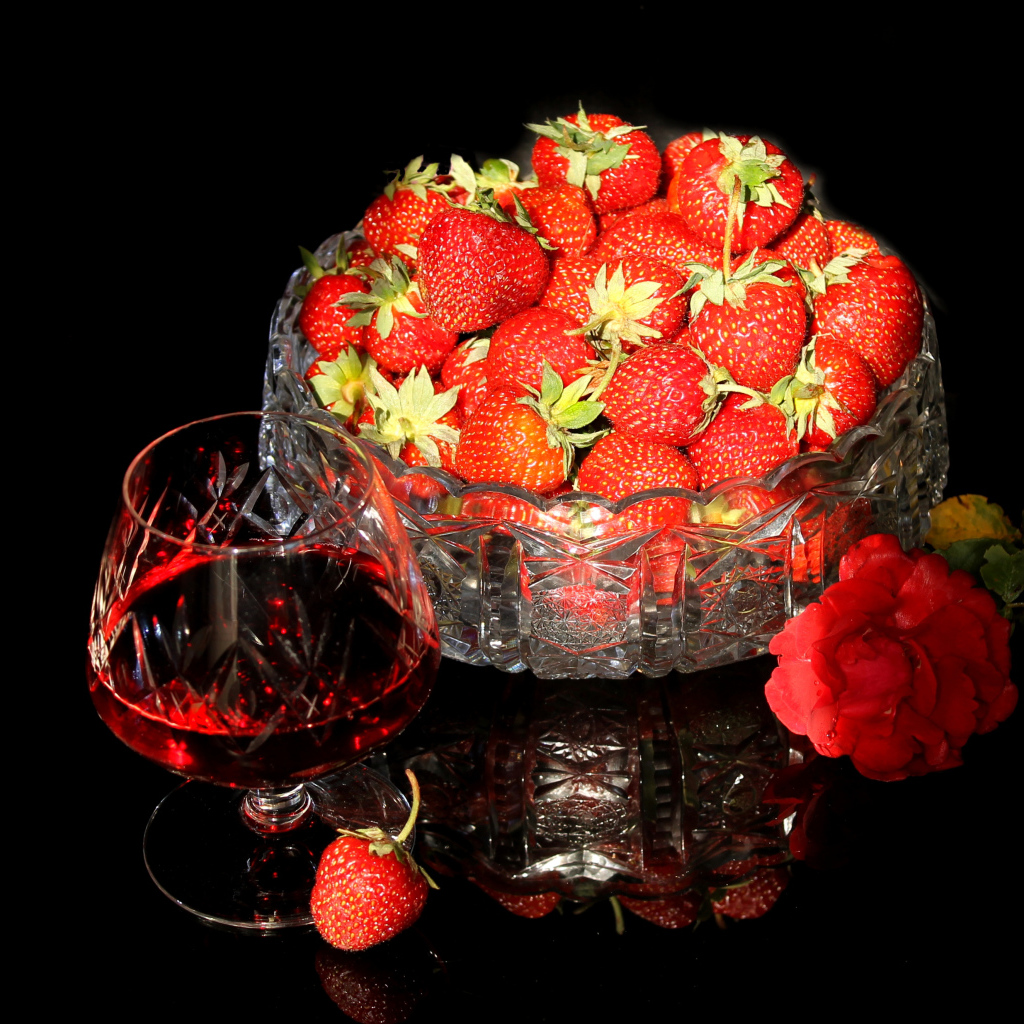 Бокал клубничного ликера на столе со спелой клубникой и красной розой