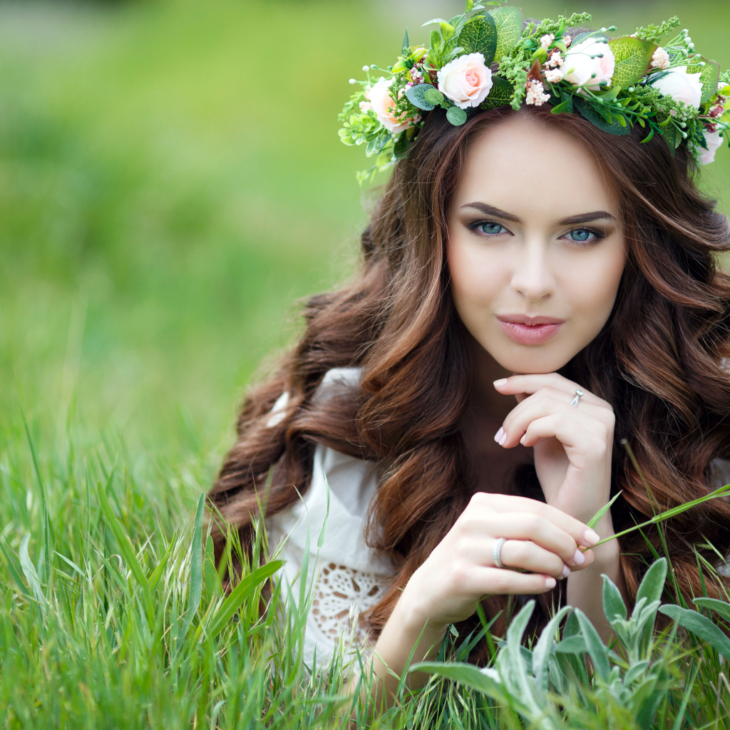 Красивая девушка шатенка с венком на голове лежит на зеленой траве