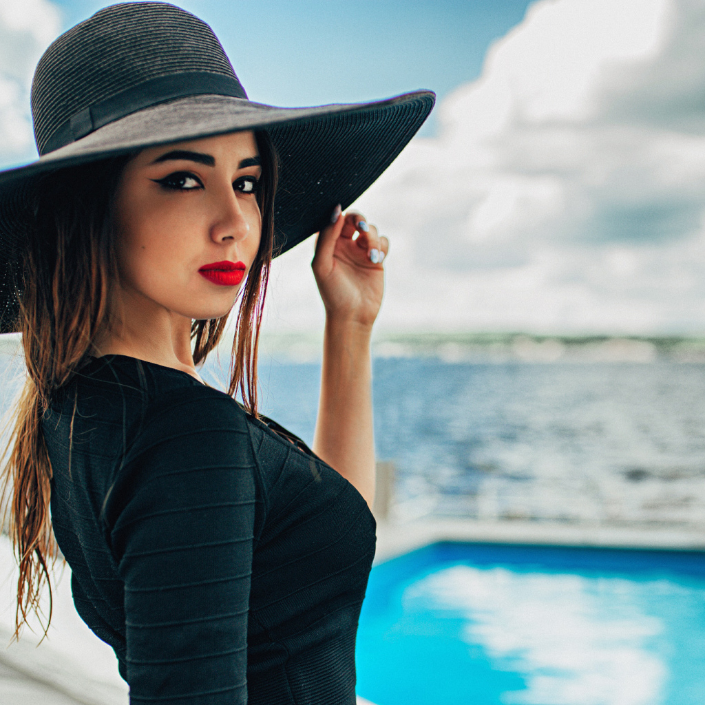 Красивая девушка в большой черной шляпе у бассейна
