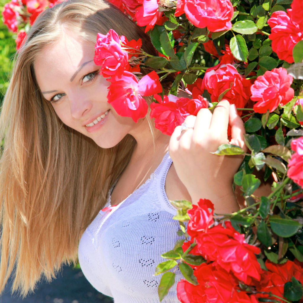Улыбающаяся девушка блондинка рядом с кустом красных роз