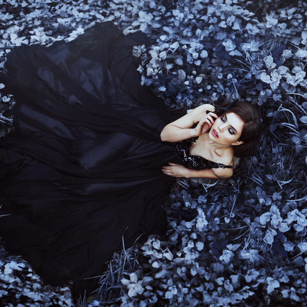 Молодая девушка модель с красивом черном платье лежит на траве