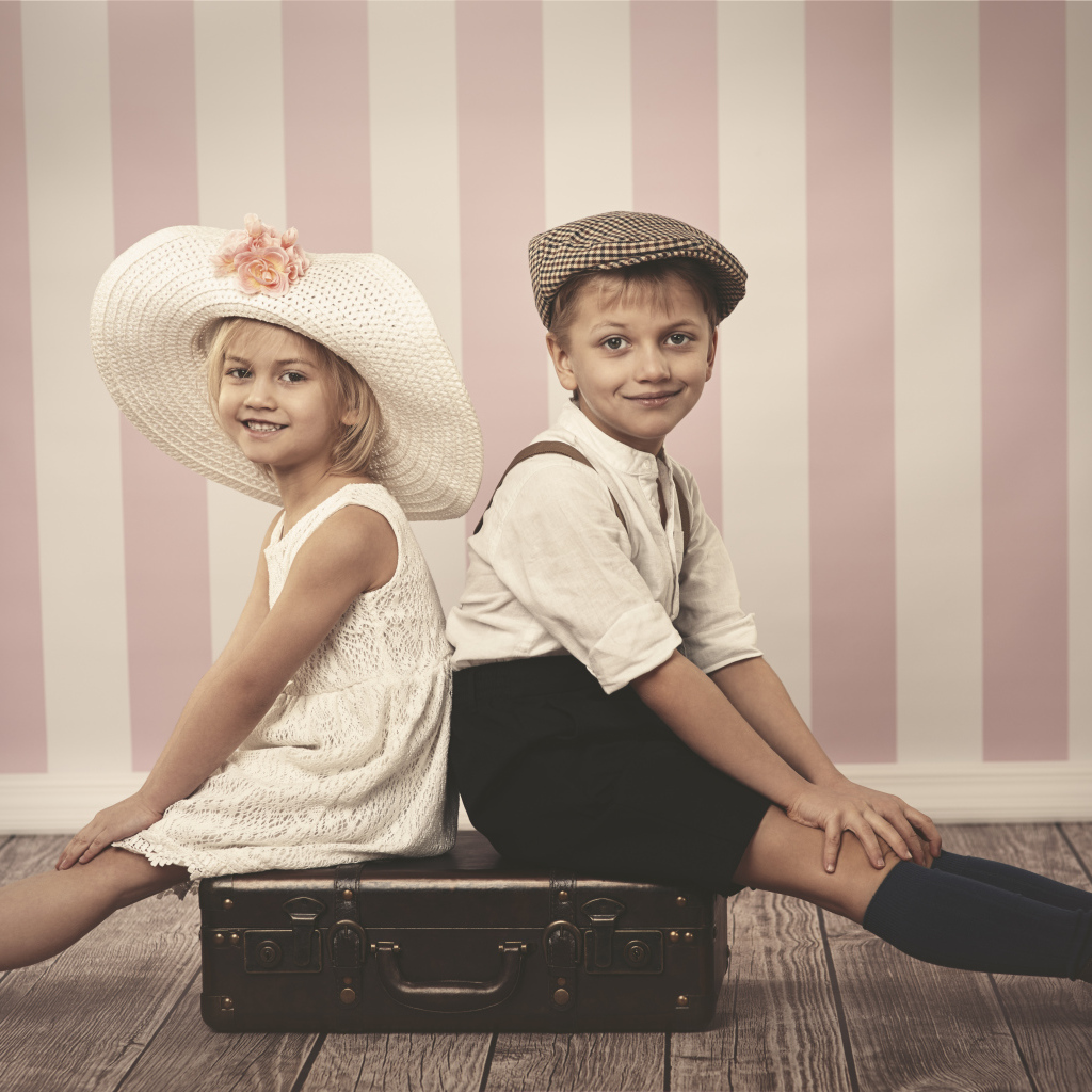 Девочка в большой белой шляпе и мальчик сидят на чемодане
