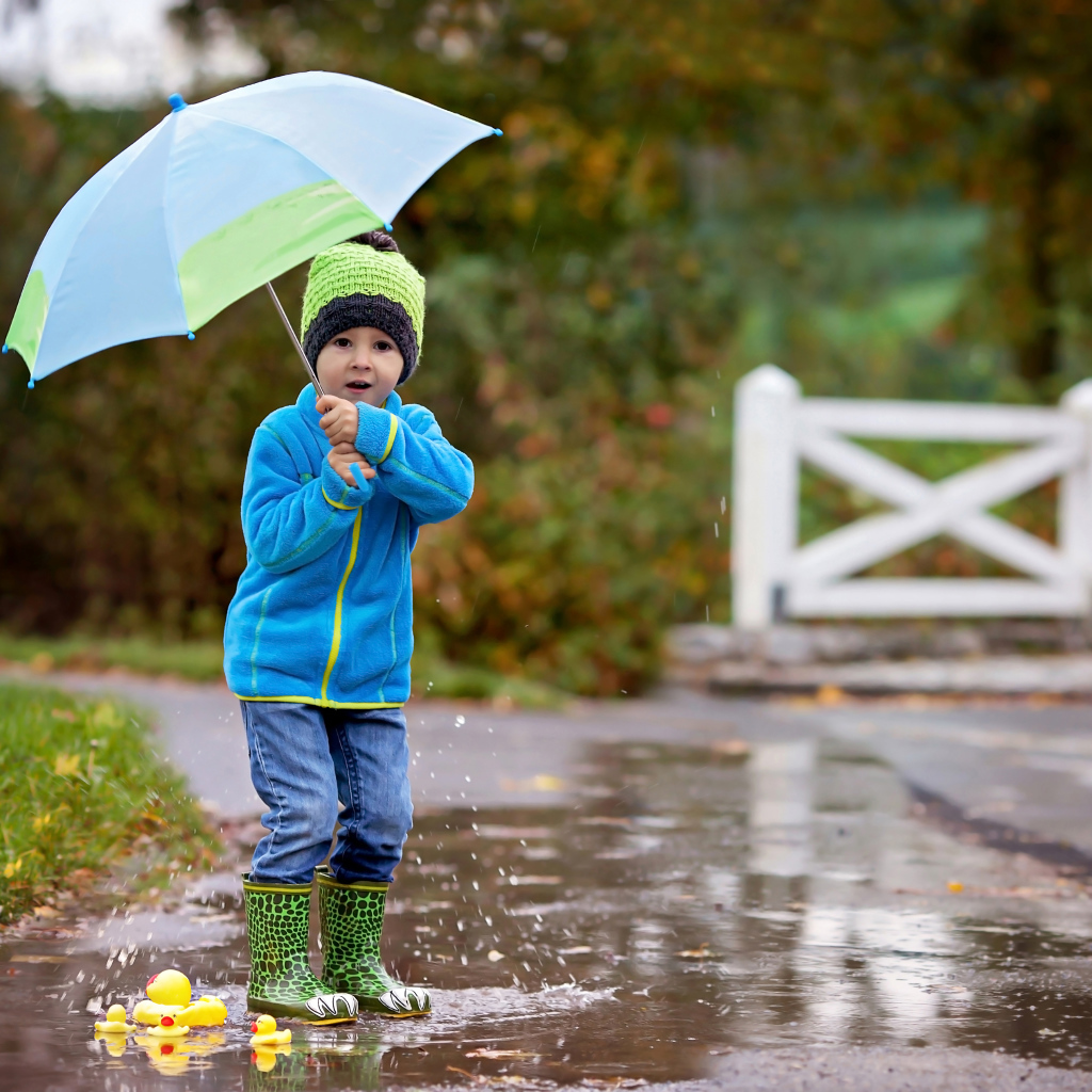 Маленький мальчик под зонтом гуляет по лужам