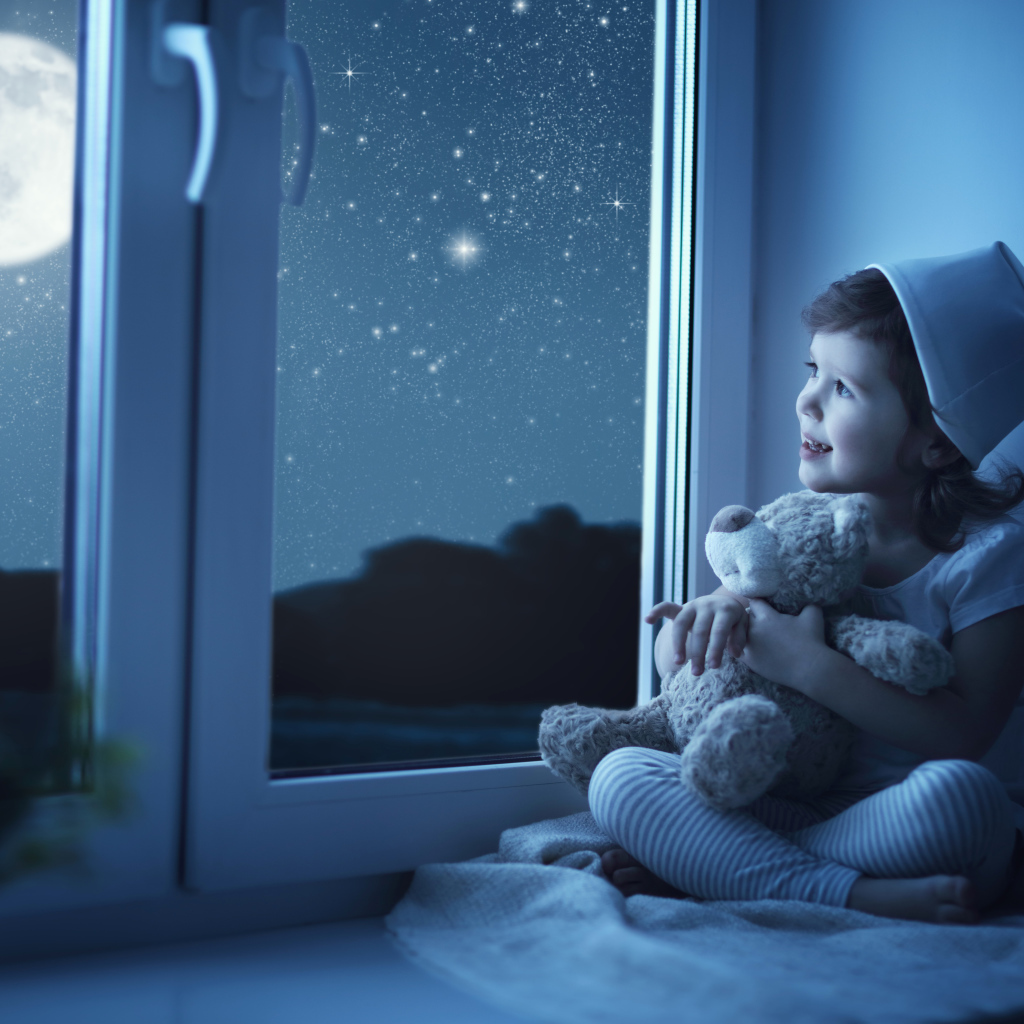 Маленькая девочка сидит на подоконнике с игрушкой ночью