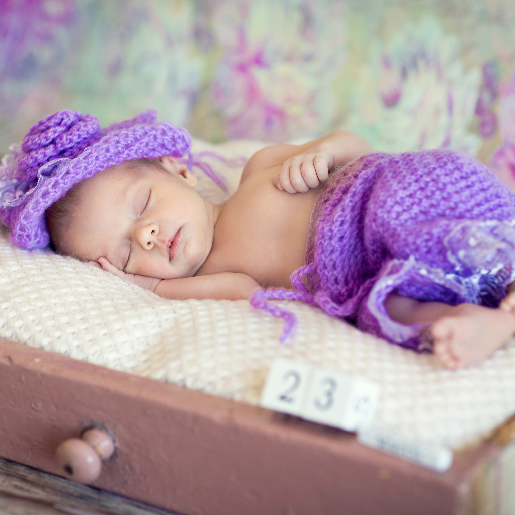 Маленький спящий младенец в вязаном фиолетовом костюме