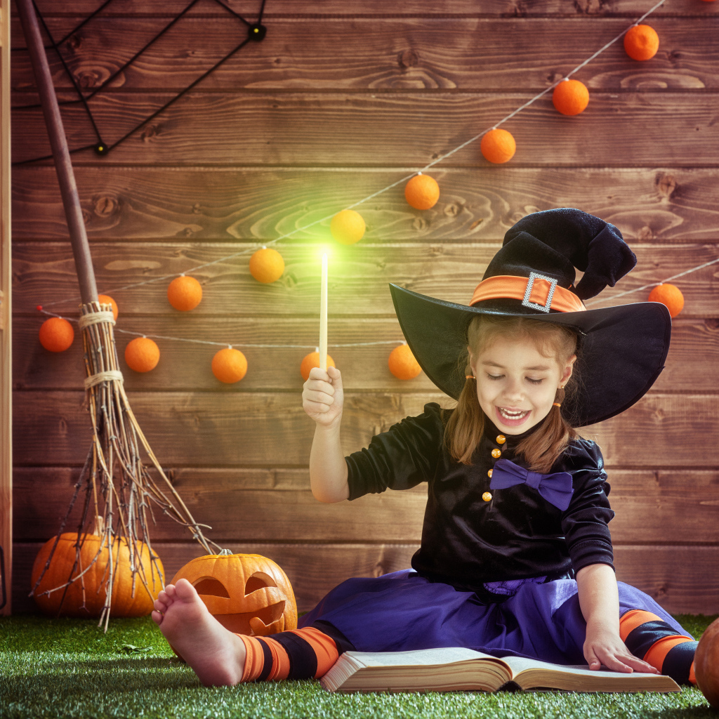 Маленькая девочка в костюме ведьмы с волшебной книгой на Хэллоуин