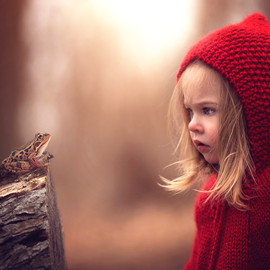 Удивленная девочка в красном капюшоне смотрит на лягушку
