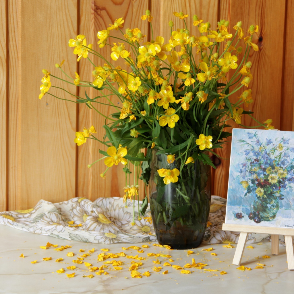 Букет желтых полевых лютиков в стеклянной вазе на столе с картиной