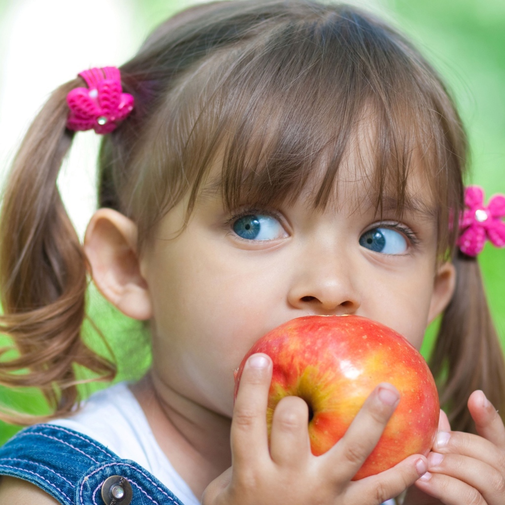 Маленькая голубоглазая девочка с большим яблоком