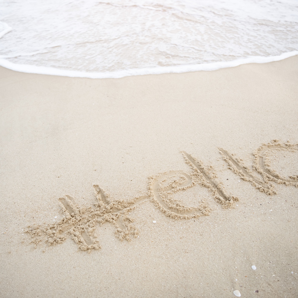 Надпись Hello на мокром песке у моря летом 