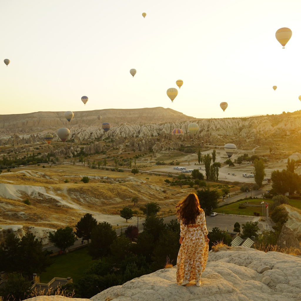 Девушка стоит на краю скалы на фоне неба с воздушными шарами