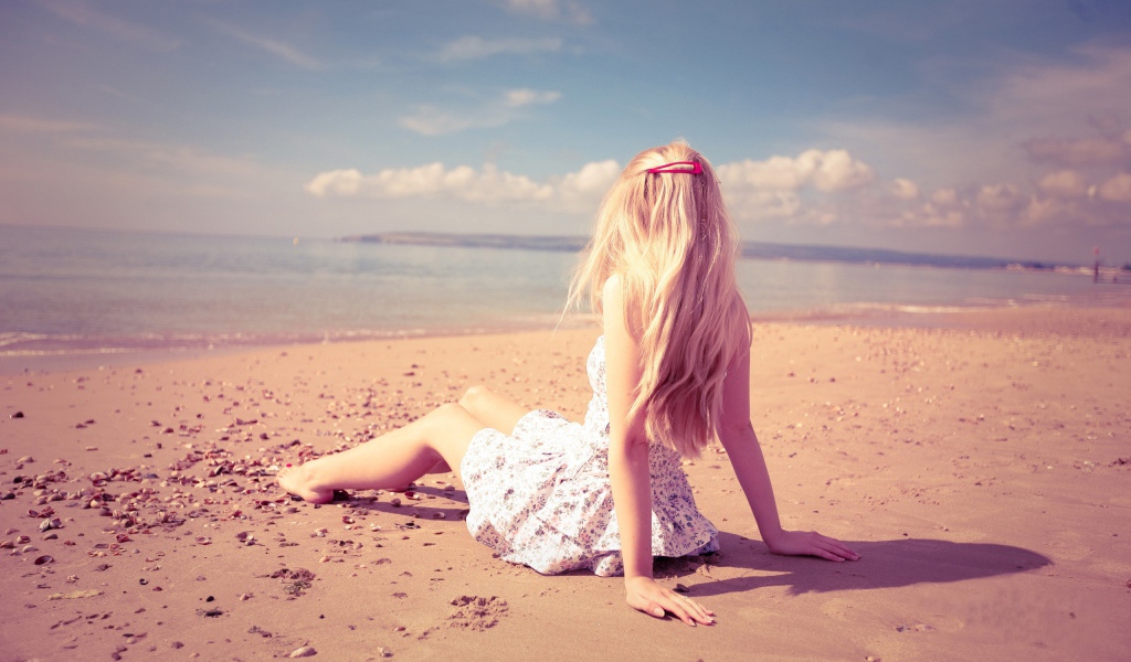Блондинка с розовой заколкой сидит на пляже
