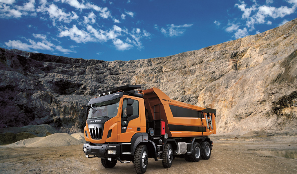 Оранжевый грузовик Astra HD9 84.50 8×4 в карьере под голубым небом
