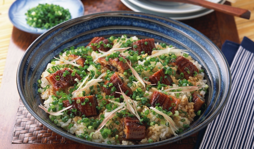 Рисовый плов с кусочками мяса и зеленым луком на столе