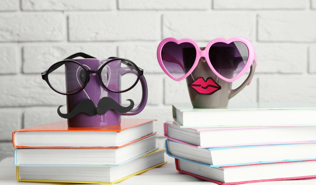 Две забавные чашки в очках стоят на книгах