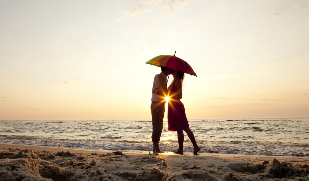 Влюбленная пара на пляже стоит под зонтом на закате