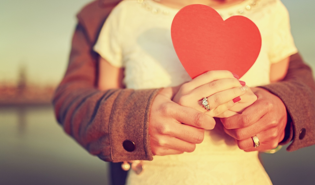 Влюбленная пара держит в руках красное бумажное сердце