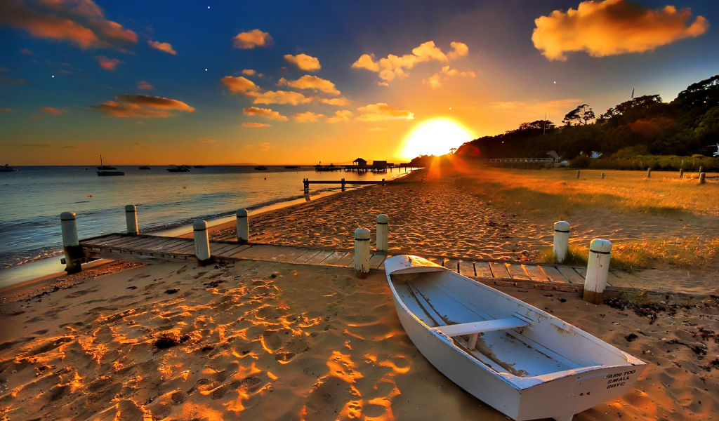 Белая лодка на пляже под закатным солнцем