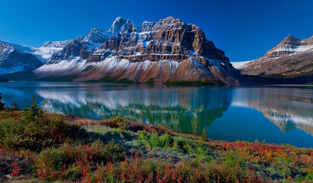 Заснеженные горы отражаются в голубой глади воды 