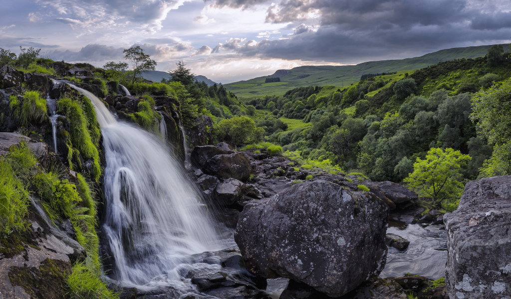 Водопад стекает по камням на фоне красивого неба и зеленого леса