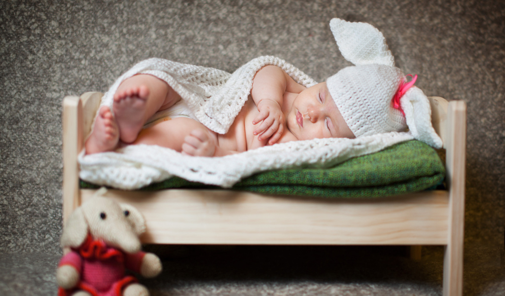 Грудной ребенок спит в деревянной кровати в белом вязаном костюме зайчика