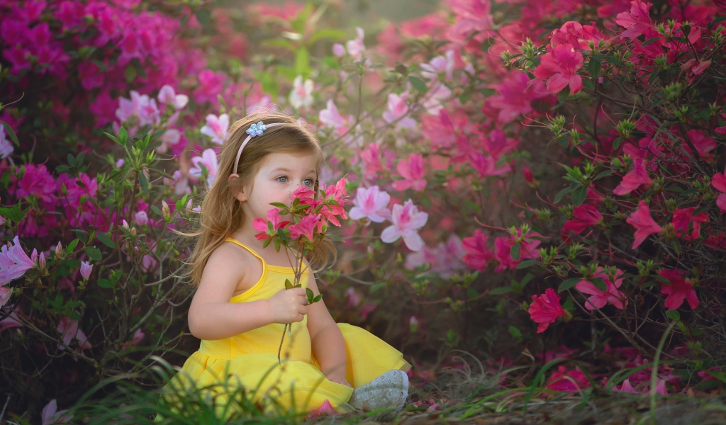 Маленькая девочка в желтом платье сидит рядом с розовыми цветами
