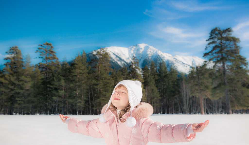 Маленькая девочка в розовой куртке на фоне гор зимой