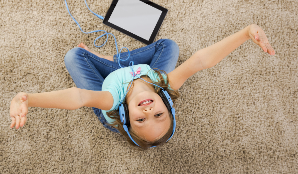 Маленькая девочка слушает музыку в наушниках сидя на ковре