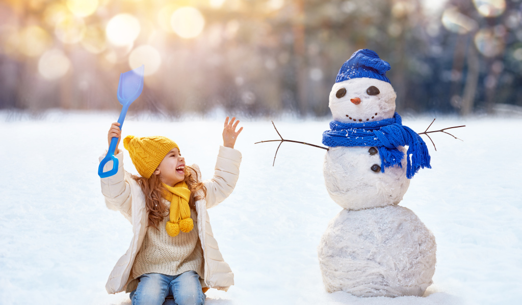 Маленькая улыбающаяся девочка со снеговиком зимой