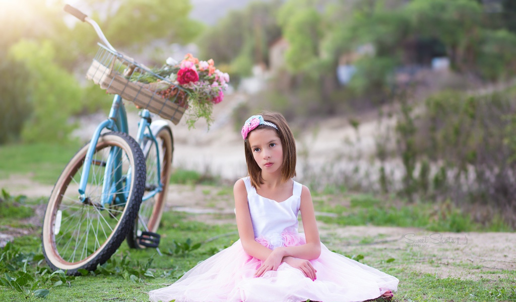 Грустная девочка в красивом платье сидит на траве с велосипедом