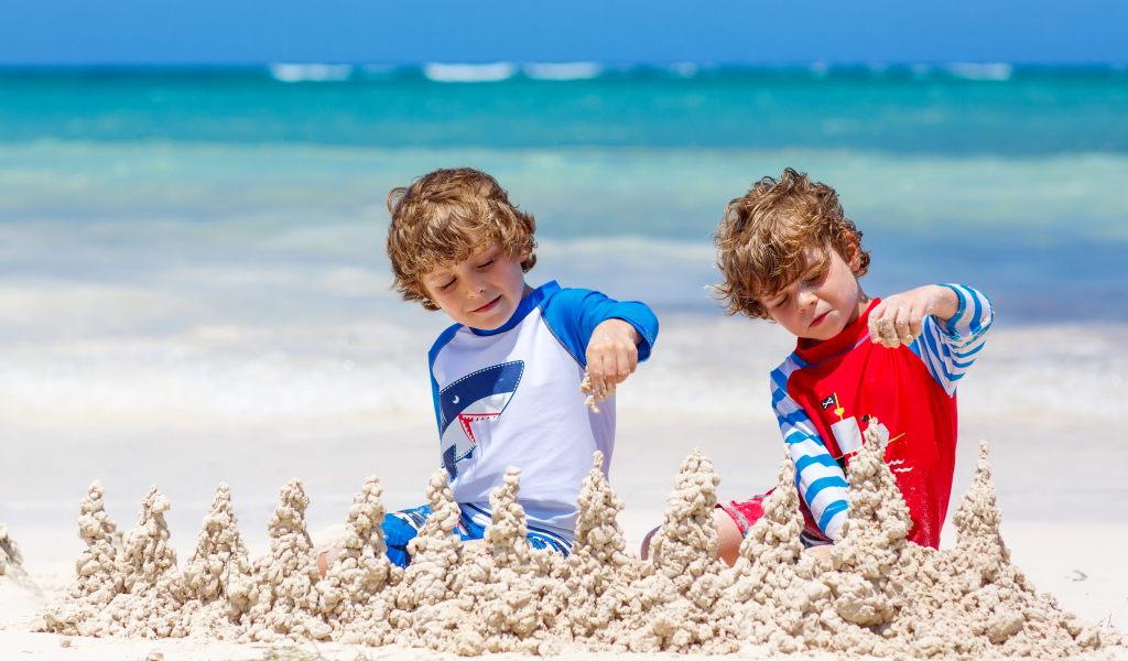Два маленьких мальчика играют с песком на пляже