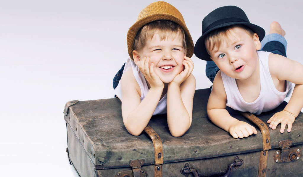 Два маленьких улыбающихся мальчика лежат на старом чемодане
