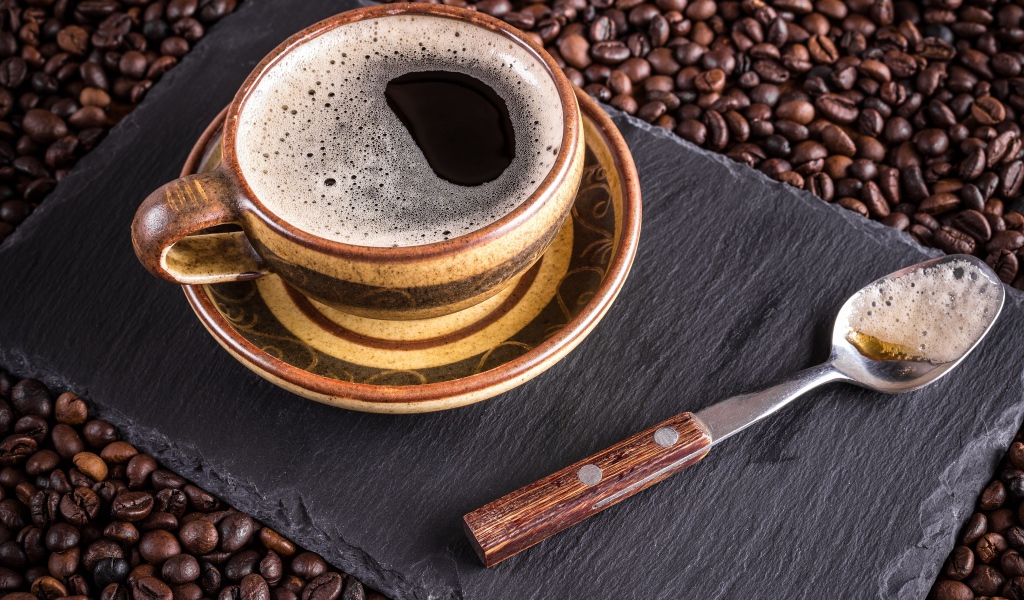 Большая чашка кофе с чайной ложкой стоят на кофейных зернах