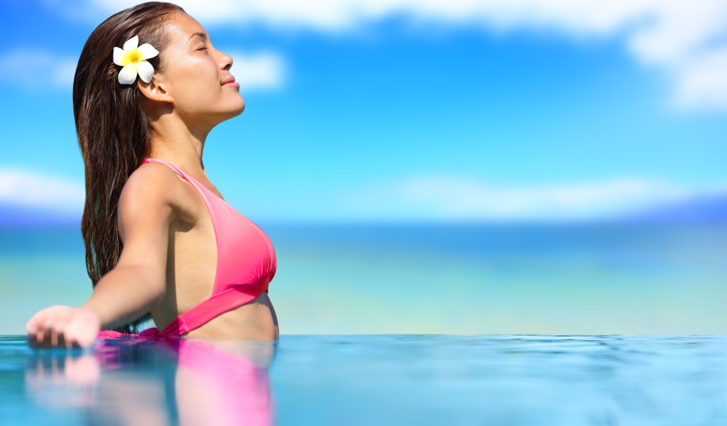 Девушка в розовом купальнике стоит в воде на солнце
