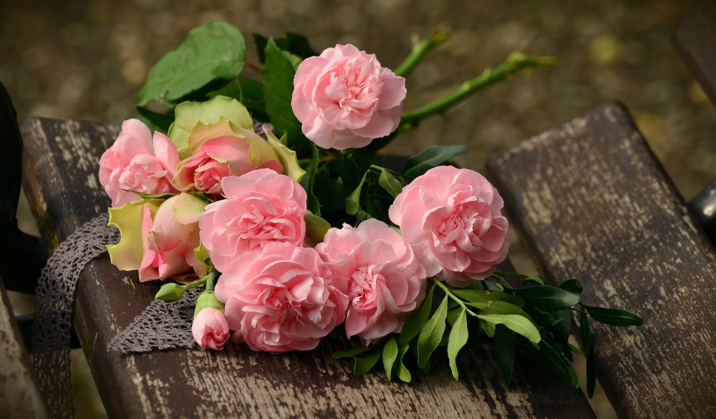 Букет красивых нежных розовых роз лежит на деревянной лавке