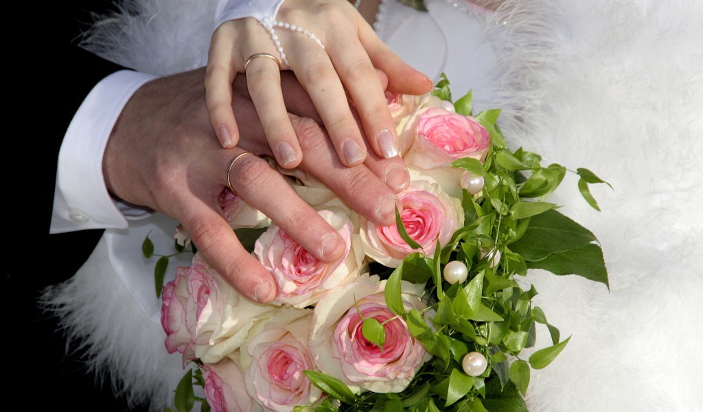 Руки жениха и невесты на букете с розовыми розами