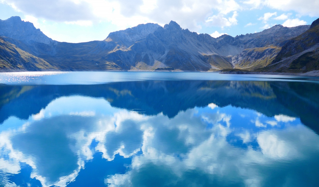 Красивые белые облака отражаются в воде озера на фоне гор 