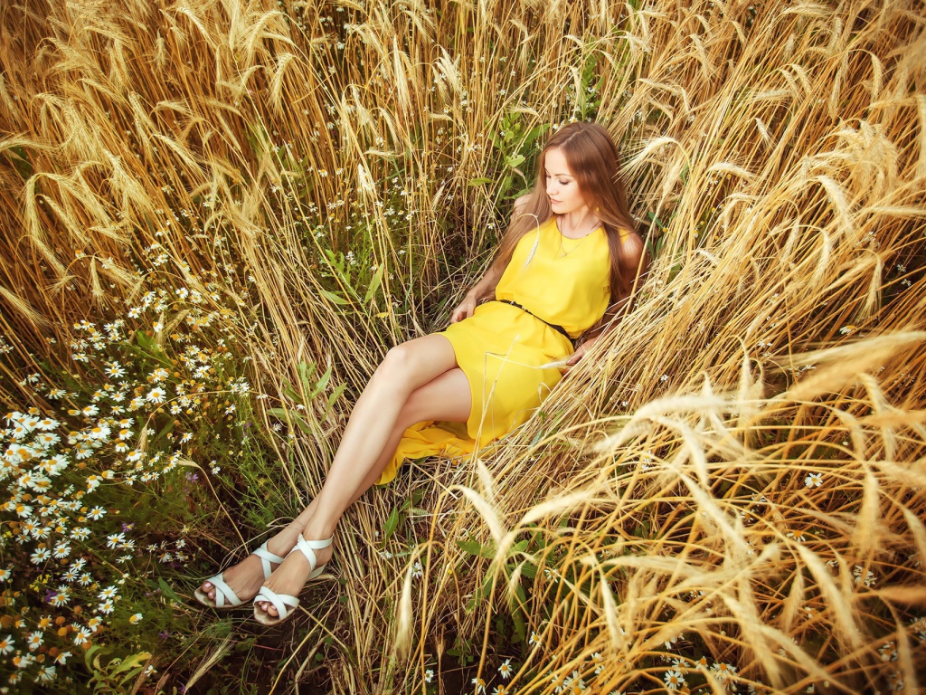 Девушка в желтом платье лежит на колосках пшеницы