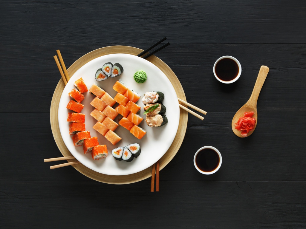 Суши и роллы на большой белой тарелке с соевым соусом