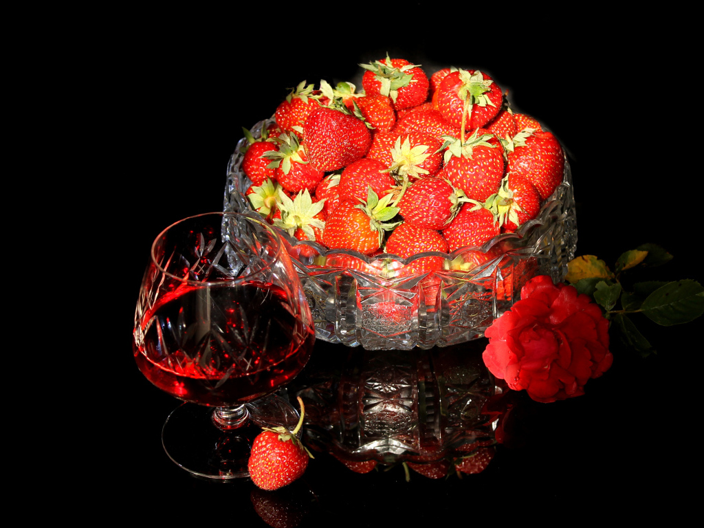 Бокал клубничного ликера на столе со спелой клубникой и красной розой