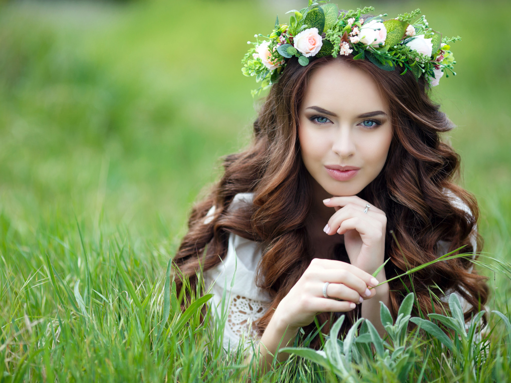 Красивая девушка шатенка с венком на голове лежит на зеленой траве