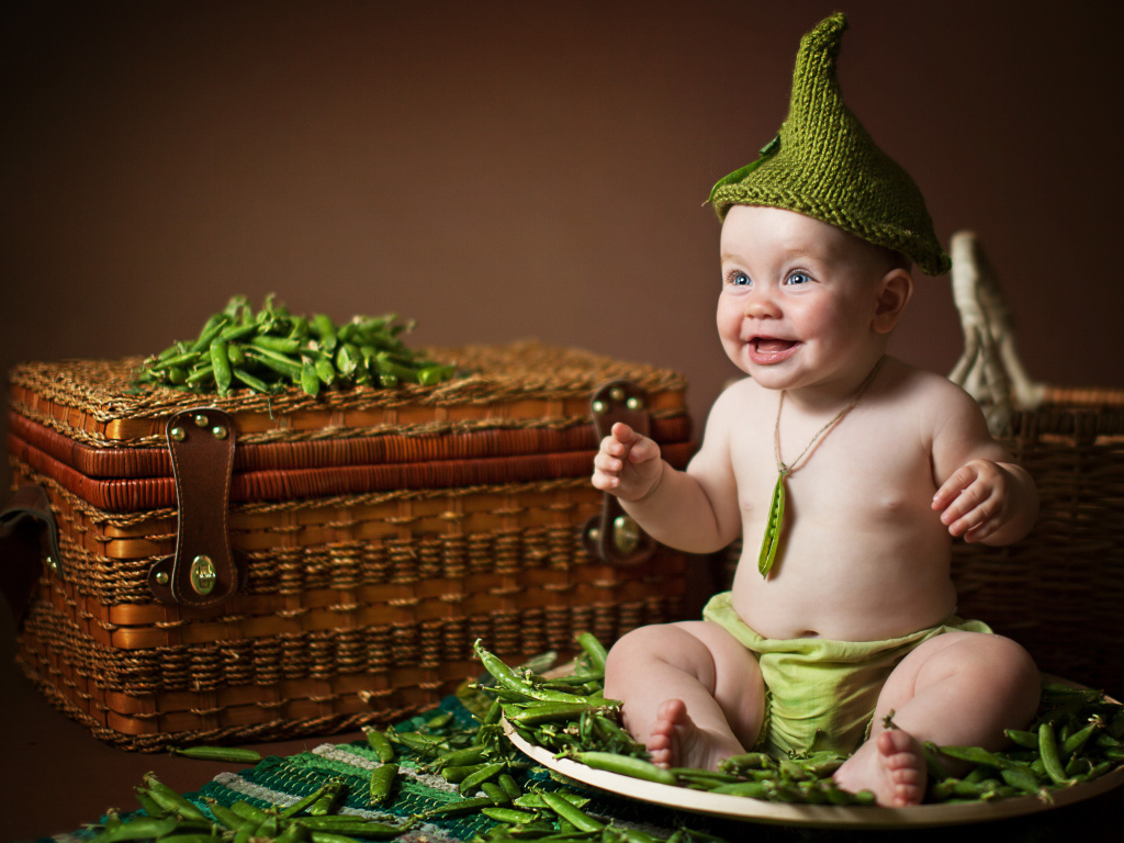 Забавный улыбающийся малыш сидит на стручках зеленого гороха