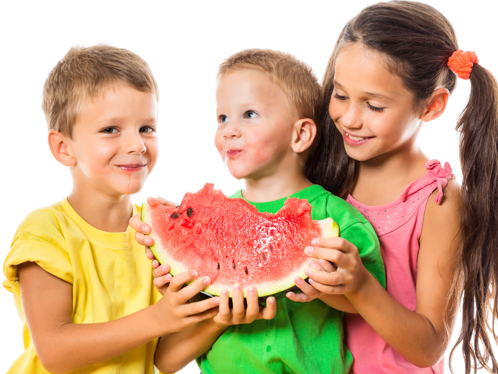 Два маленьких мальчика и девочка едят арбуз на белом фоне